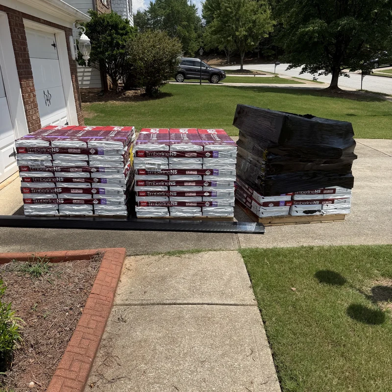 Three pallets of GAF Timberline NS shingles and accessories on a residential driveway.