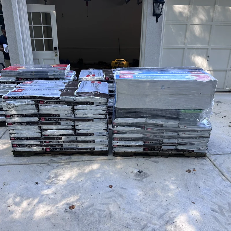 GAF Camelot II shingle bundles and wrapped roofing accessories on a protected driveway.