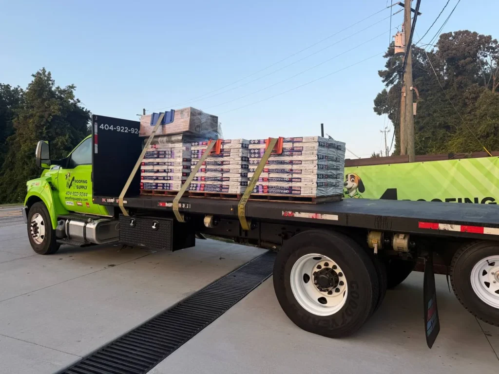 Pallets of shingle bundles secured with straps on an A+ Roofing Supply flatbed truck.