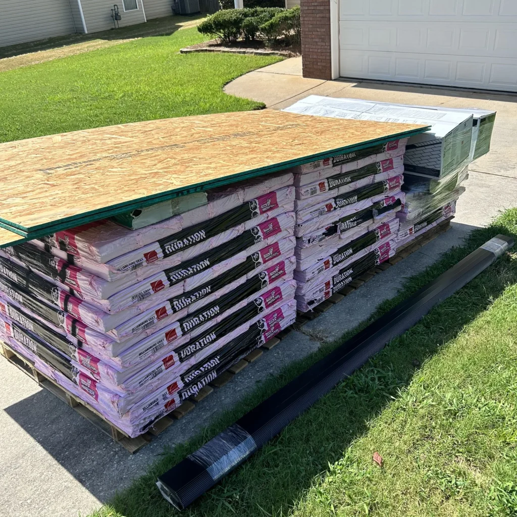 Owens Corning Duration shingle bundles topped with OSB sheets on a residential driveway.